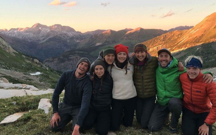 A group of people smile for a photo in front of a vast mountainous landscape. 